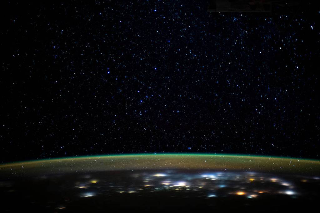 Stars glitter in the night sky above Earth’s atmospheric glow