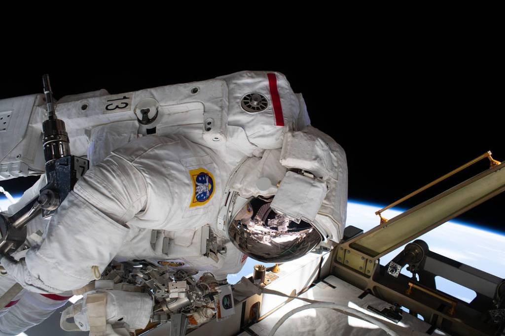 The reflection in Jessica Meir’s spacesuit helmet is Christina Koch