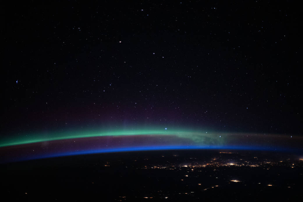 An aurora above the city lights and a beneath a starry sky