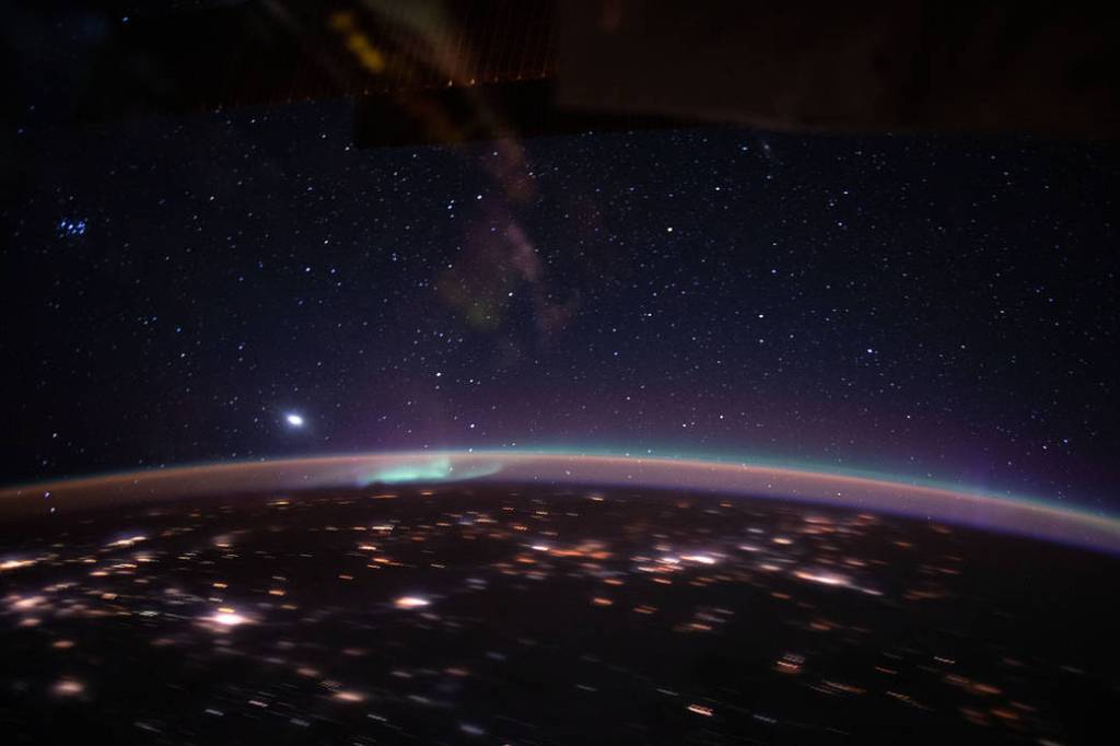 An aurora accents Earth’s atmospheric glow underneath a starry sky