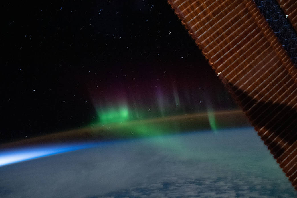 A wispy "aurora australis" intersects with the Earth's airglow