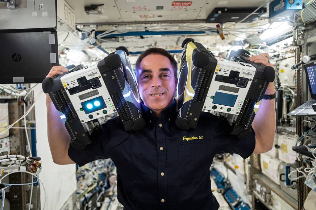 Astronaut Chris Cassidy poses with two Astrobee robotic assistants