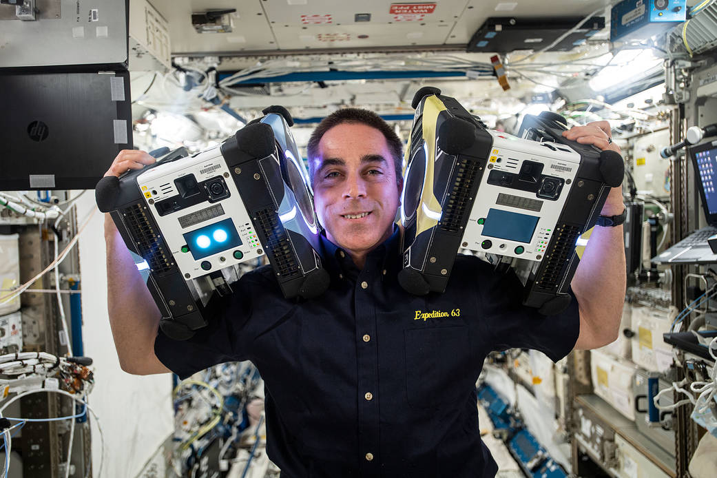 Astronaut Chris Cassidy poses with two Astrobee robotic assistants