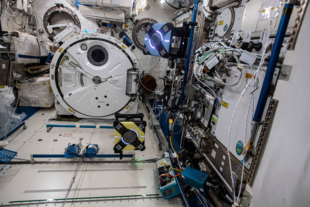 A pair of Astrobee robotic assistants are pictured flying around