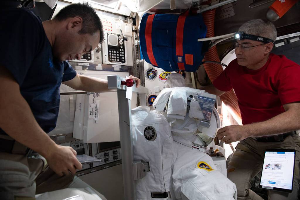 Astronauts Akihiko Hoshide and Mark Vande Hei work on a U.S. spacesuit