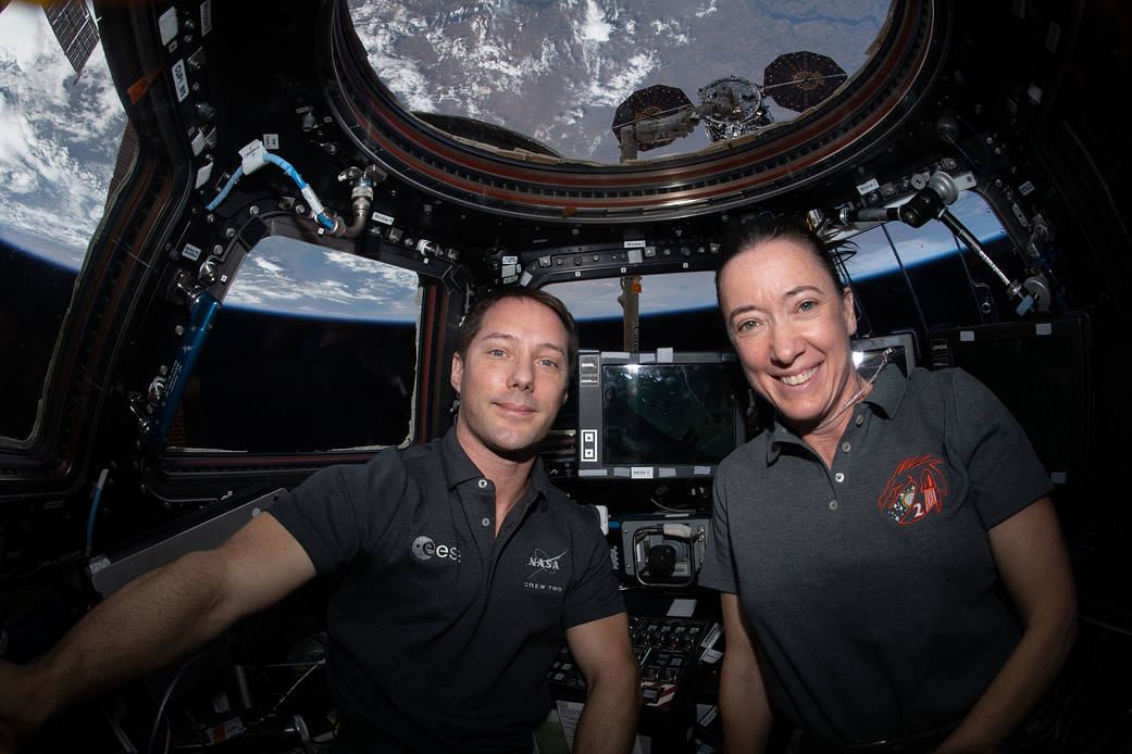 Astronauts Thomas Pesquet and Megan McArthur are inside the cupola with the Northrop Grumman Cygnus space freighter just outside behind them.