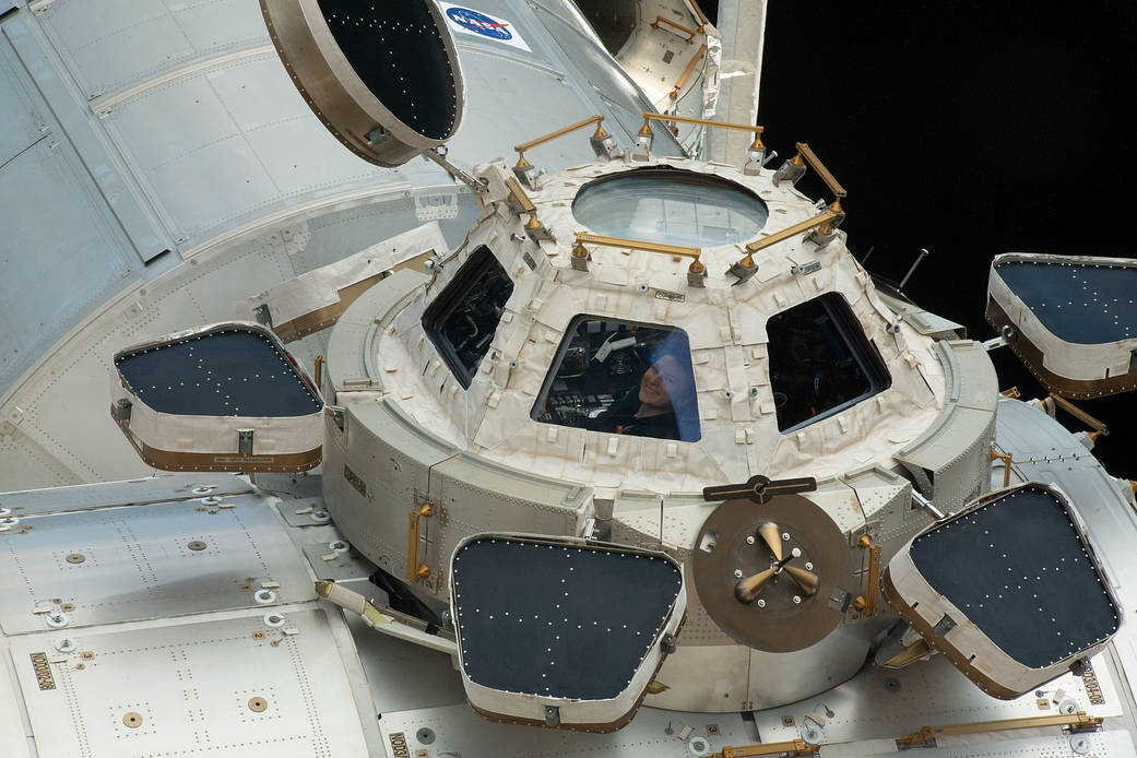 Astronaut Kayla Barron smiles while peering out from a cupola window