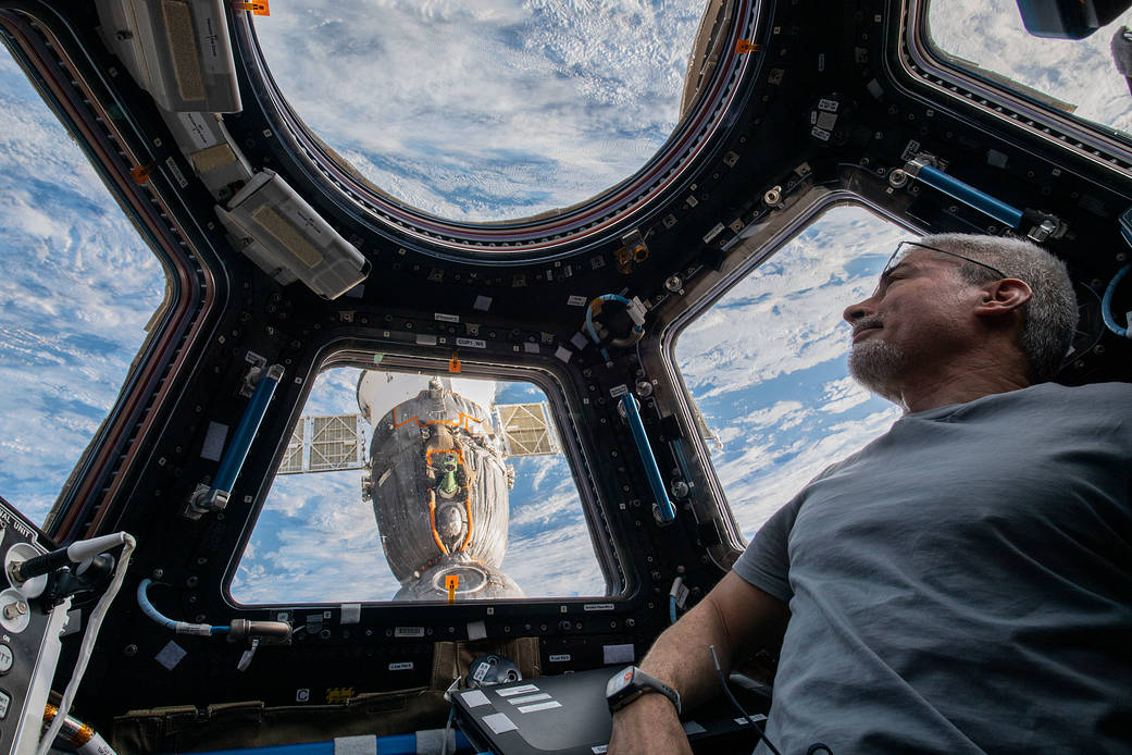 astronaut peers at the Earth below looking through the cupola windows