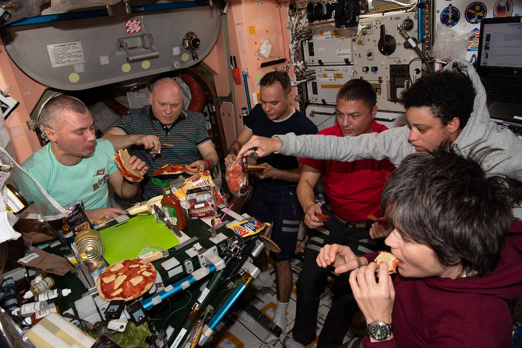 Expedition 67 crew members enjoy pizza during dinner time