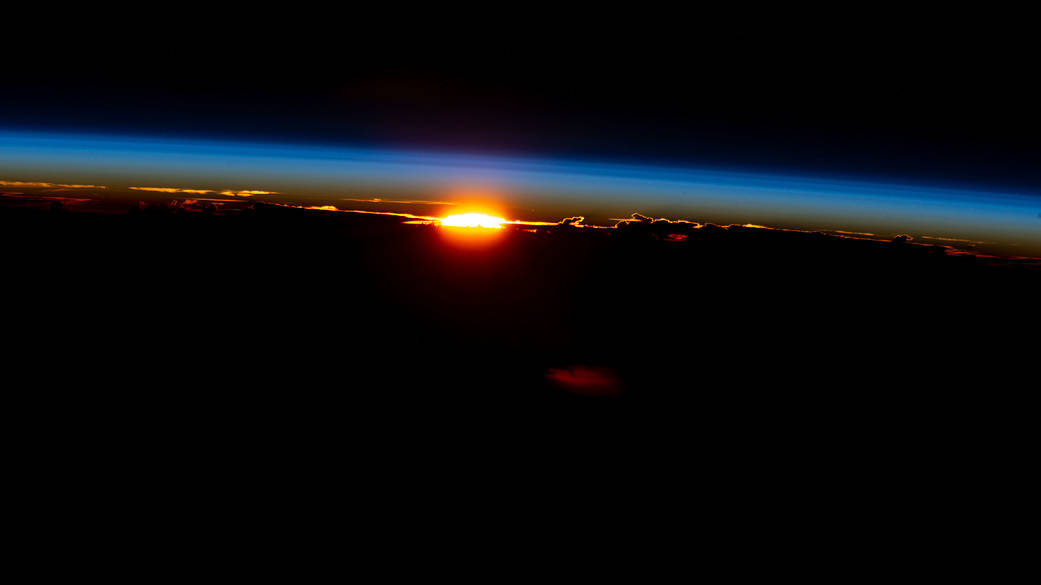 The sun sets illuminating the cloud tops and Earth's atmosphere