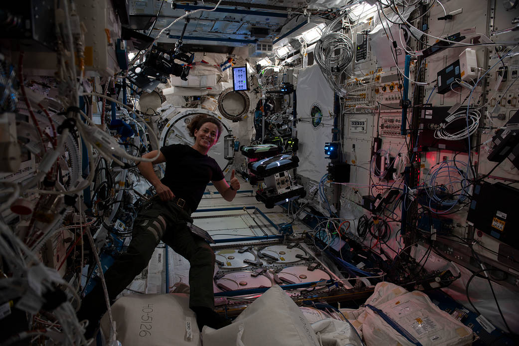 Astronaut Nicole Mann poses with a pair of Astrobee robotic helpers