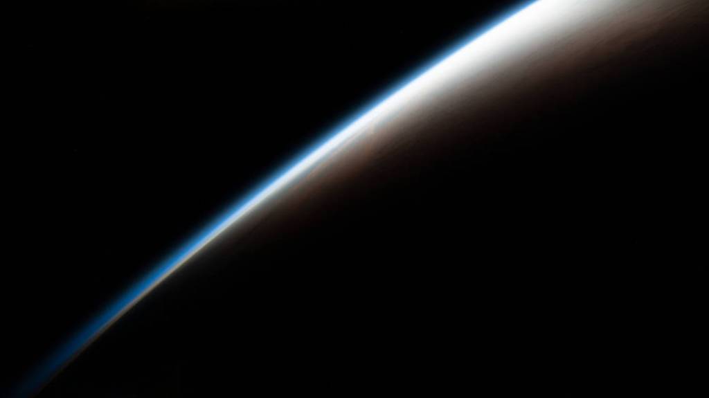 An orbital sunrise begins illuminating Earth’s atmosphere