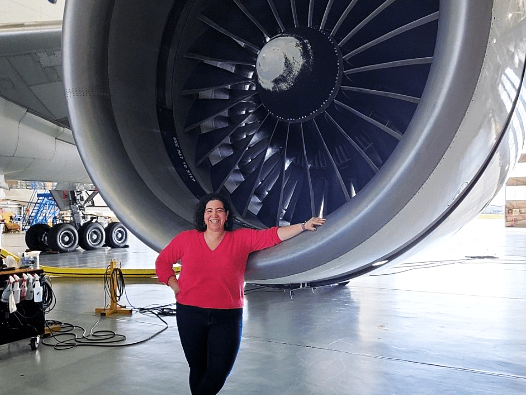 A woman poses in front of an airplane engine.