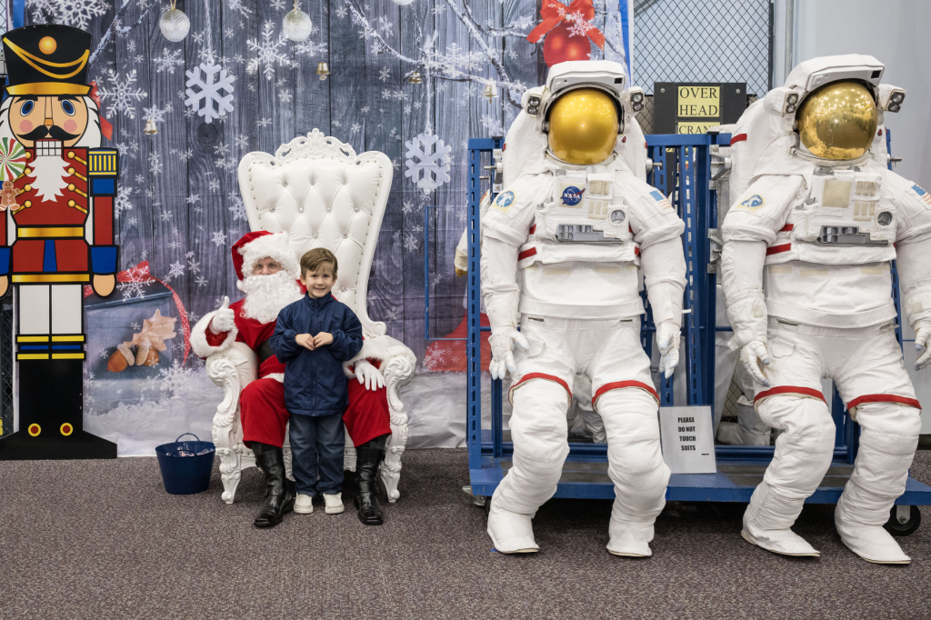 a child sitting on Santa's lap next to space suits.