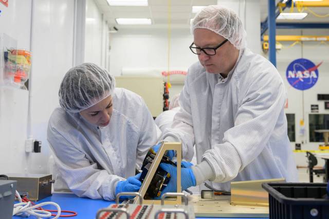Two people in white lab coats in a clean room make adjustments to the NIRVSS instrument.