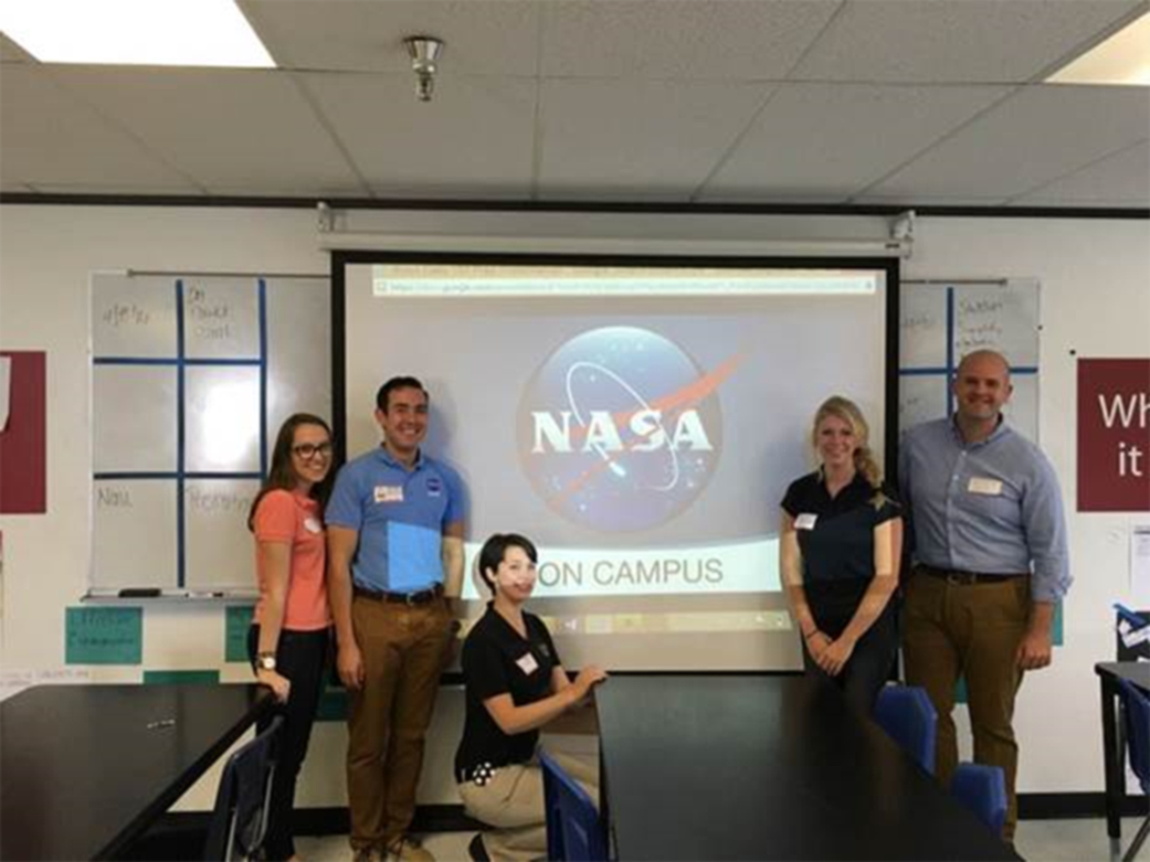 NASA interns in a classroom, in front of a screen with the image of the NASA "meatball"