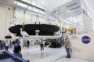 Inside the Neil Armstrong Operations and Checkout Building high bay at NASA’s Kennedy Space Center in Florida, technicians assist as a crane lifts the Orion heat shield for Artemis-1 away from the base of its shipping container.