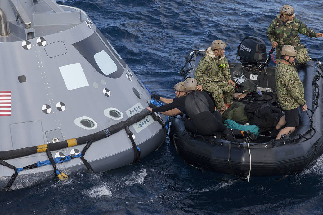 U.S. Navy divers and other personnel in a Zodiac boat secure a harness around a test version of the Orion crew module during Underway Recovery Test 5 in the Pacific Ocean off the coast of California. 