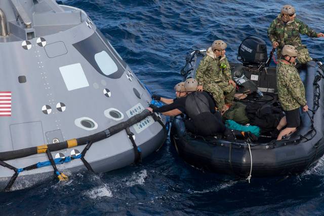 U.S. Navy divers and other personnel in a Zodiac boat secure a harness around a test version of the Orion crew module during Underway Recovery Test 5 in the Pacific Ocean off the coast of California. 