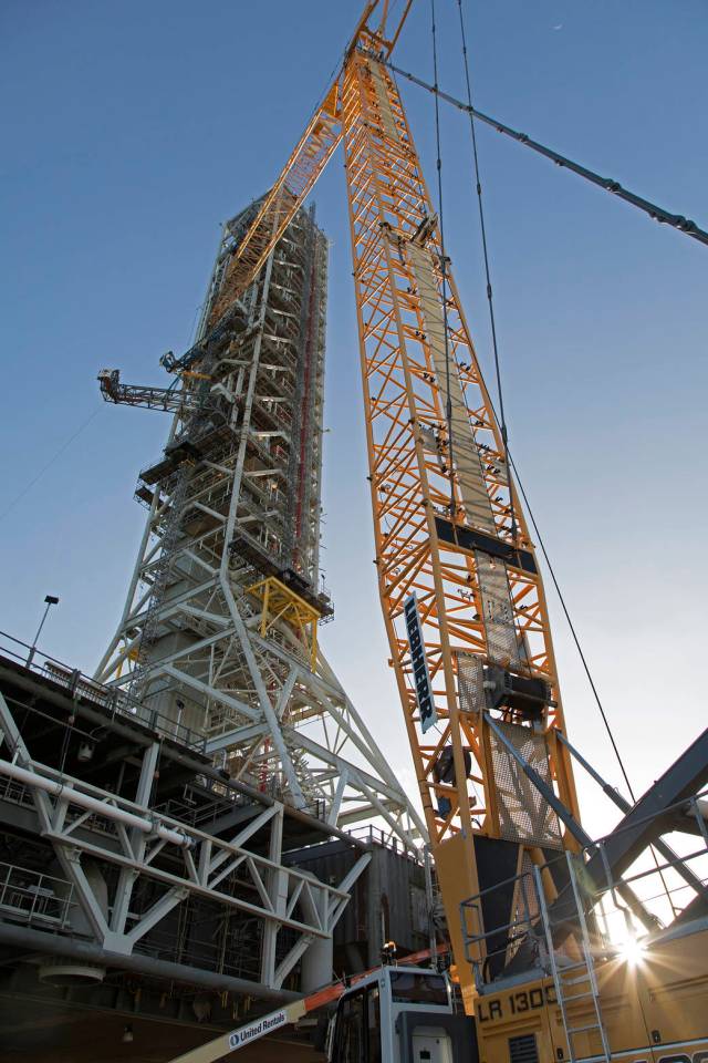 High up on the mobile launcher (ML) tower at NASA's Kennedy Space Center in Florida, construction workers assist as a crane moves the Core Stage Inter-tank Umbilical (CSITU) into place for a fit check of the attachment hardware. 