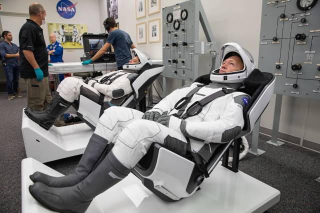 NASA astronauts Doug Hurley, foreground, and Bob Behnken don SpaceX spacesuits in the Astronaut Crew Quarters at Kennedy Space Center in Florida on Jan. 17, 2020.