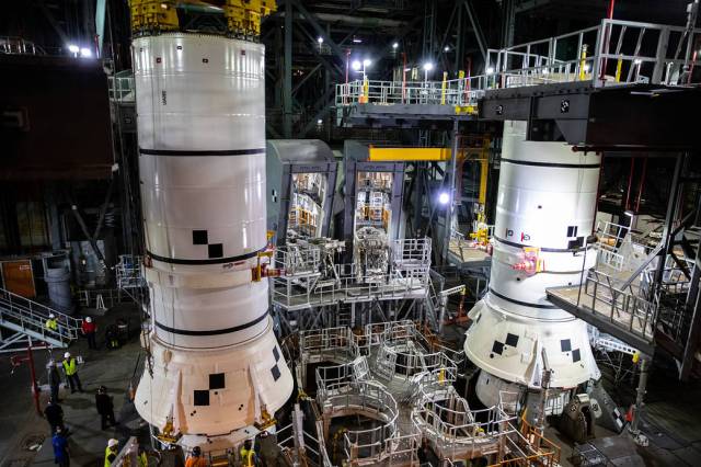 In the Vehicle Assembly Building at Kennedy Space Center, workers help secure the second of two Artemis I aft booster segments for the Space Launch System rocket onto the mobile launcher. 