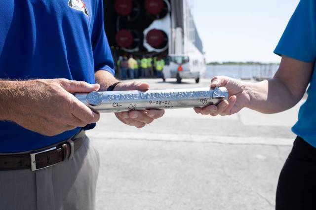 The Space Launch System program heralds the arrival of the SLS core stage with a symbolic “passing of the baton” to NASA’s Exploration Ground Systems, making the transition into final preparations for flight.