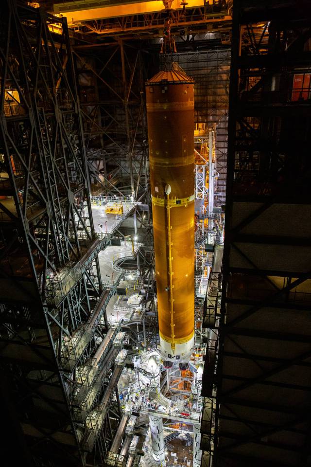 The Space Launch System core stage - the largest part of the rocket - is lowered onto the mobile launcher, in between the twin solid rocket boosters, inside the Vehicle Assembly Building.