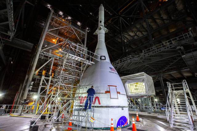 The Artemis I Orion spacecraft, secured on the Space Launch System (SLS) and enclosed in its launch abort system, is in view high up in High Bay 3 of the Vehicle Assembly Building.