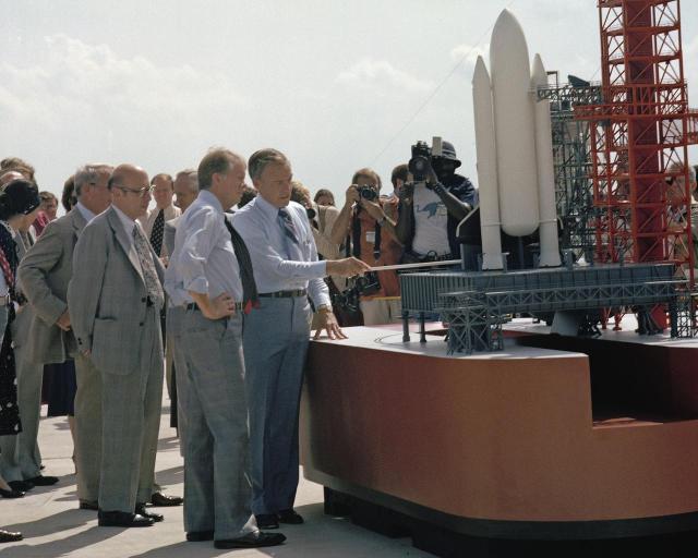 President Jimmy Carter, hand on waist, is briefed on preparations for the first space shuttle launch by center director Lee Scherer.