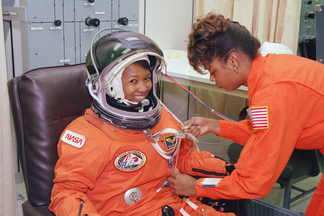 NASA astronaut in orange flight suit assisted by technician on launch day