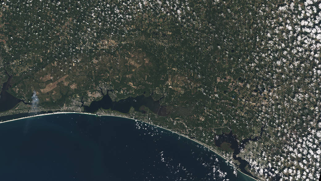 The white sands of Pensacola Beach stand out in this Landsat 9 image of the Florida Panhandle of the United States, with Panama City visible under some popcorn-like clouds.
