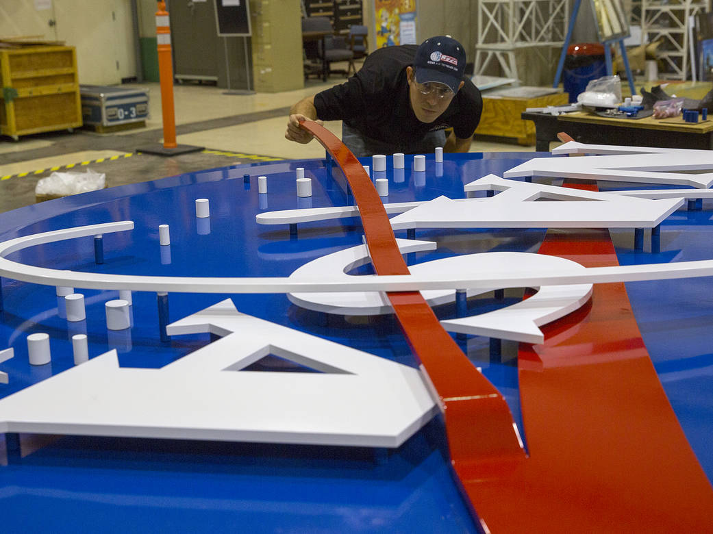 In this photo, technician Christopher Rex puts final touches on an 8-foot diameter NASA logo.
