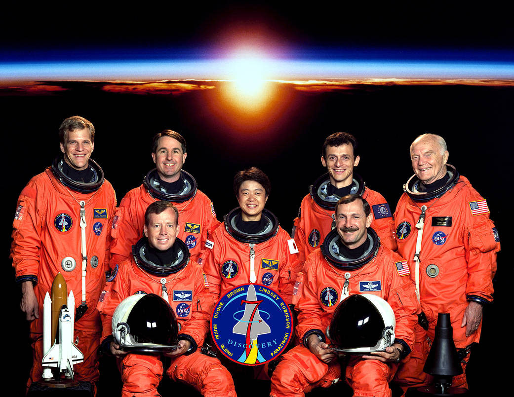 Seven astronauts pose for portrait in orange spacesuits