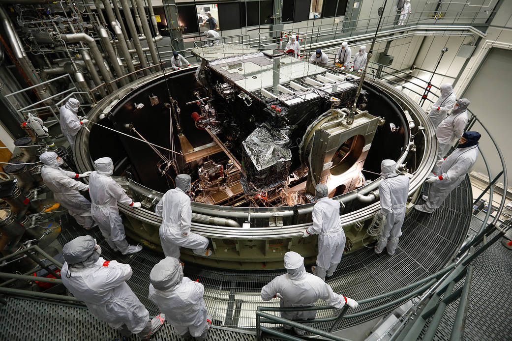 technicians lower satellite into large round chamber