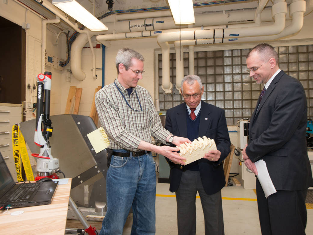 A man shows a cast of a 3D ice shape to another man while another looks on.