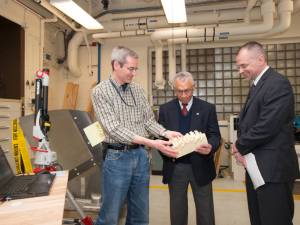 A man shows a cast of a 3D ice shape to another man while another looks on.