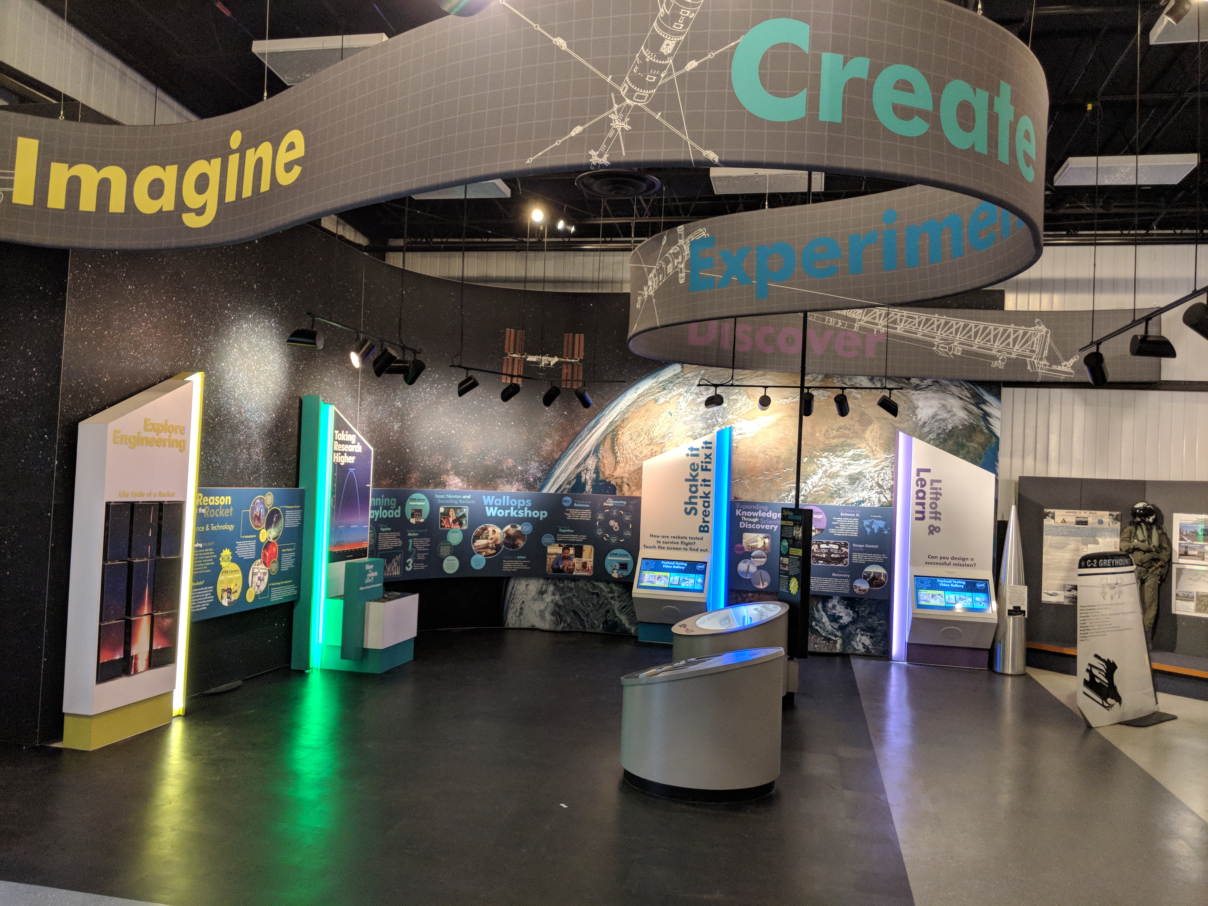 A gray banner with the words Imagine, Create, Experiment and Discover hangs above a colorful exhibit with panels with information about engineering and sounding rockets