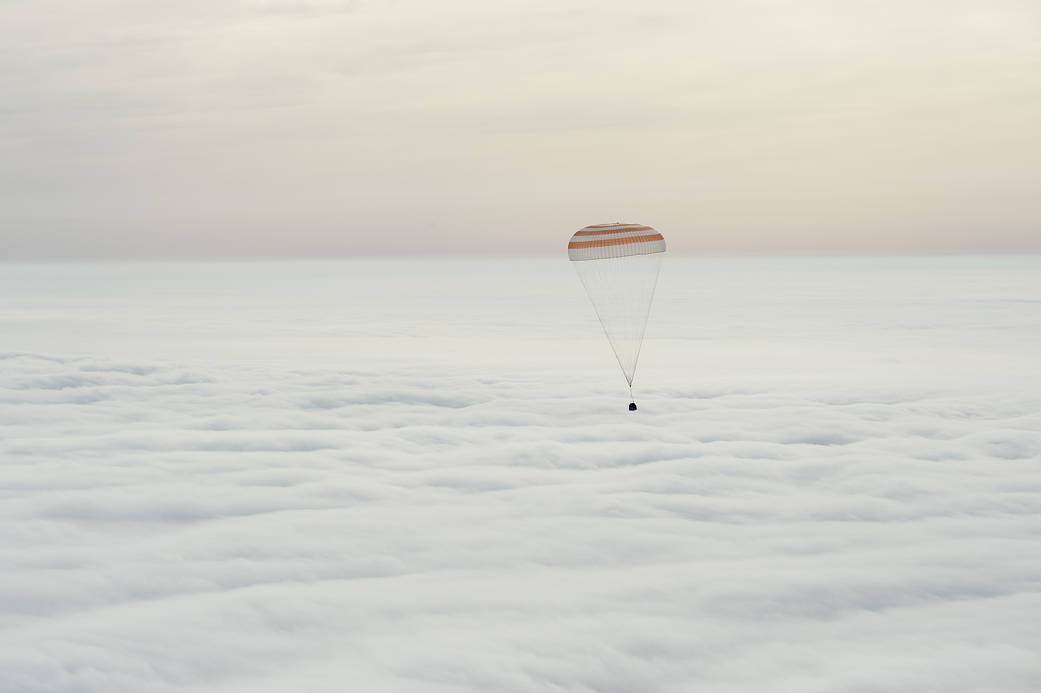 Soyuz capsule with parachute deployed descends through clouds on the way to landing