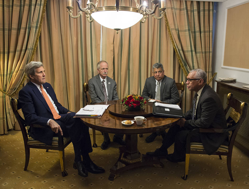 The four representatives sit down at a table in a gold hue room with a lamp overhead.