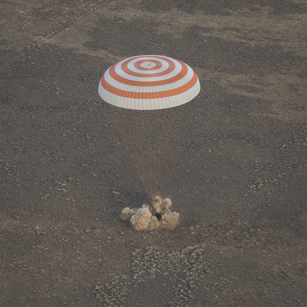 Soyuz touches down with parachute overhead