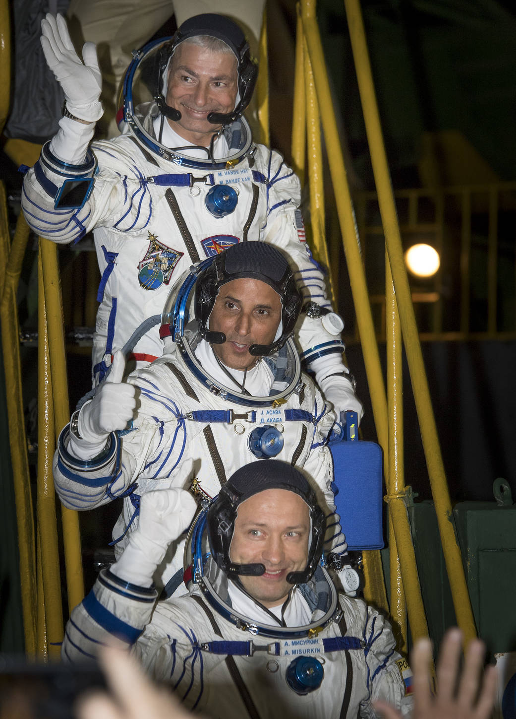 Three astronauts in Sokol suits wave farewell before boarding Soyuz