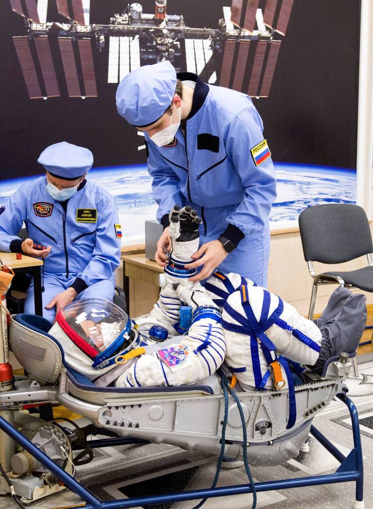 Mark Vande Hei of NASA is assisted with his glove during suit check