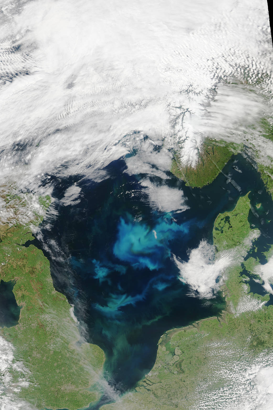 Bloom of greenish blue phytoplankton in dark blue waters with clouds overhead