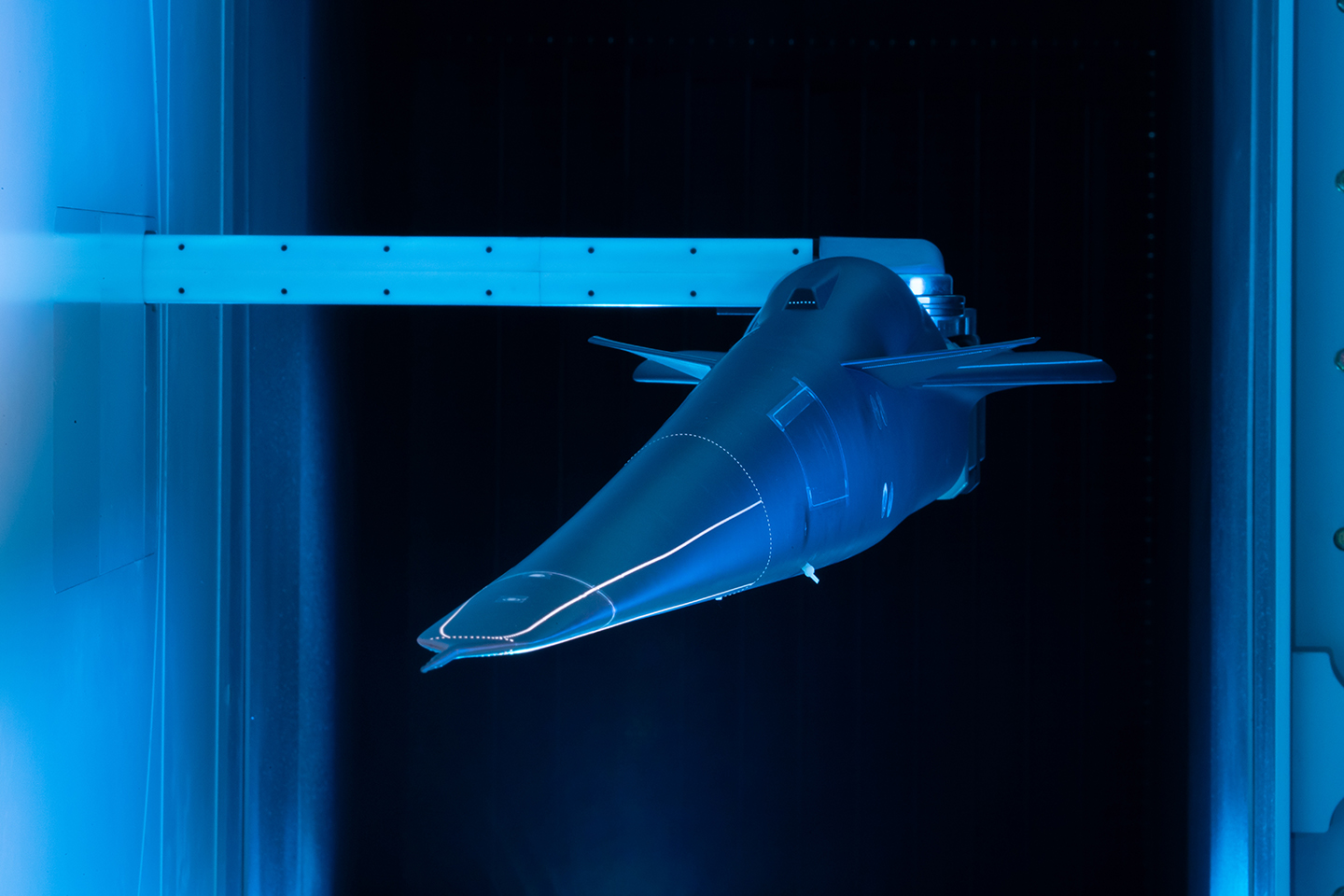 Model of the X-59 in a wind tunnel with blue lighting.