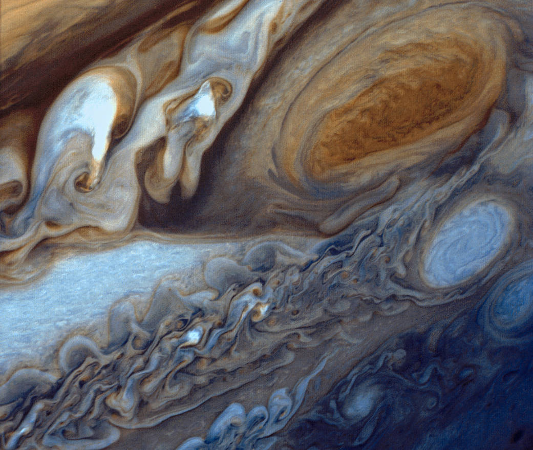 Jupiter's Great Red Spot  is a swirl of orange-brown, lightening to pale orange at the outer edges. To its left are brown, white, and orange swirls; at bottom, blue and white swirls and ripples. The entire image has the effect of dyes dripped into water.