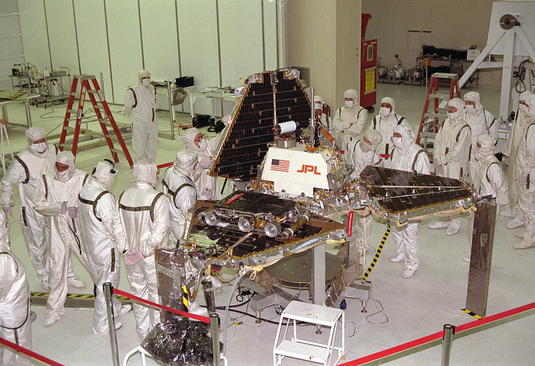 Mars Pathfinder spacecraft set up in room with technicians in clean suits at work