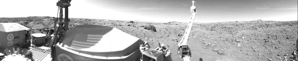 Wide view of Mars surface in black and white with part of Viking lander and arm at left of frame