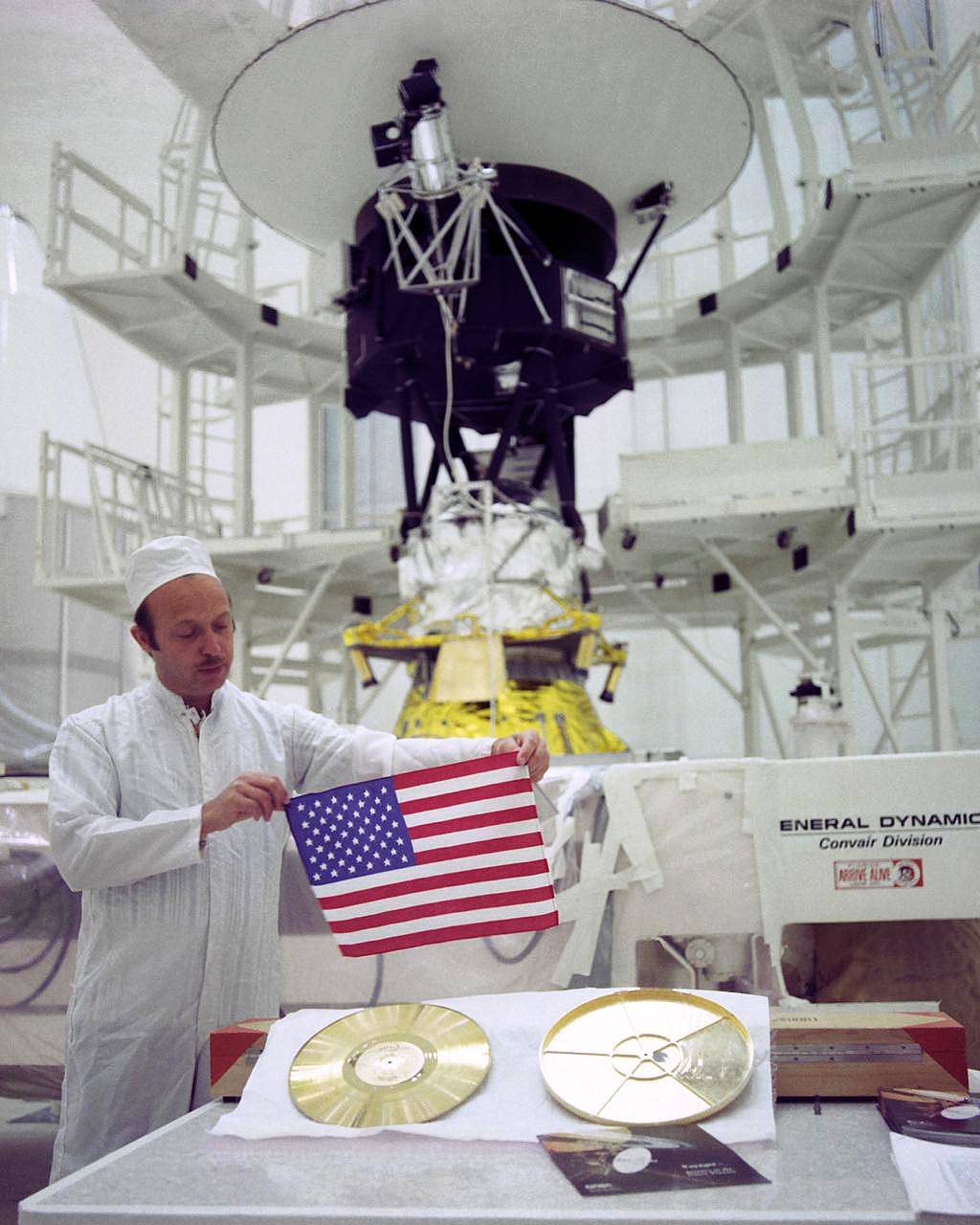 Technician holds American flag in front of Voyager spacecraft and Golden Record with case