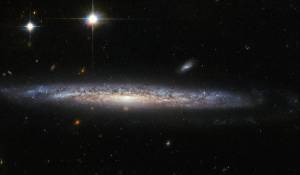 edge on galaxy with foreground stars and background spirals